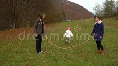 年轻的母亲在秋林里和孩子们玩耍。小美女跳绳。一家人很幸福。